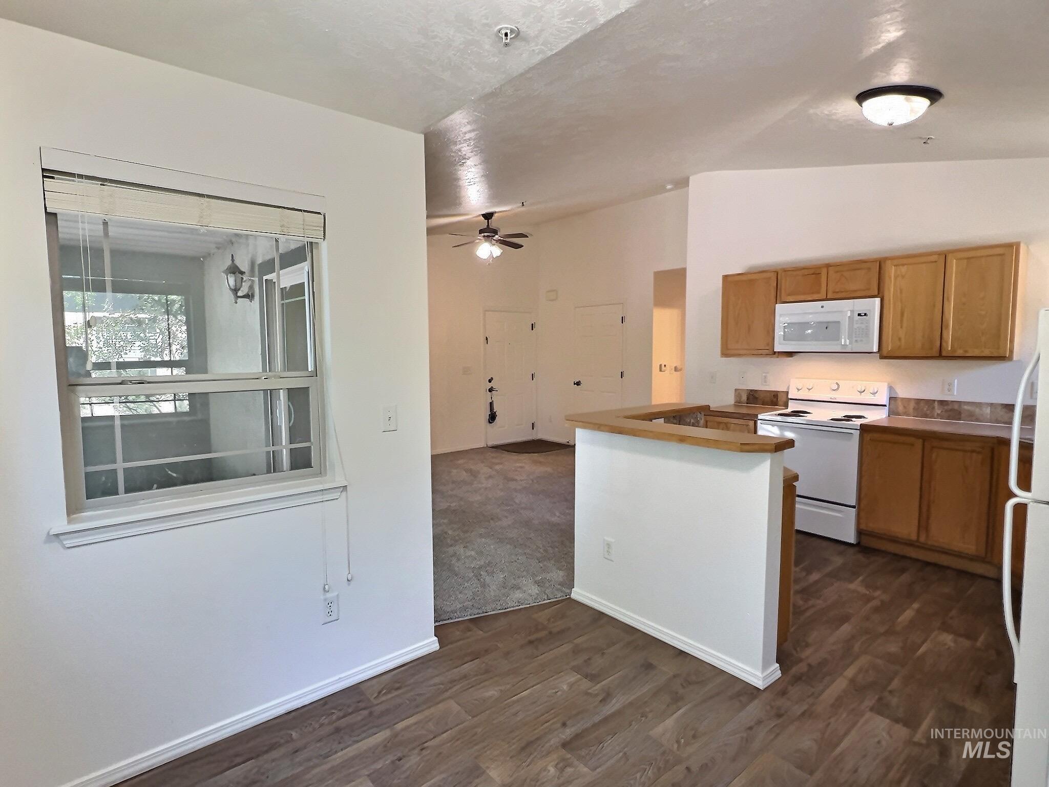 Kitchen with white appliances, dark wood-style floors, open floor plan, a ceiling fan, and light countertops