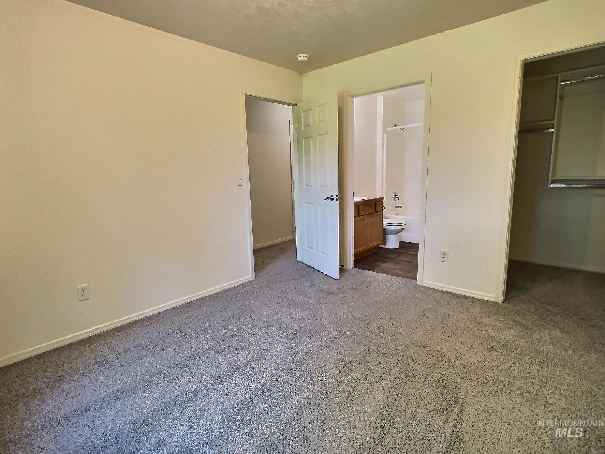 Unfurnished bedroom featuring a spacious closet, carpet flooring, and ensuite bathroom