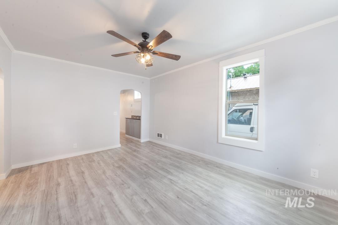 Spare room with crown molding, light wood-style floors, arched walkways, and a ceiling fan
