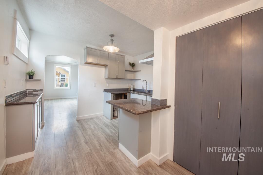 Kitchen featuring open shelves, light wood-type flooring, a textured ceiling, a peninsula, and dark stone countertops