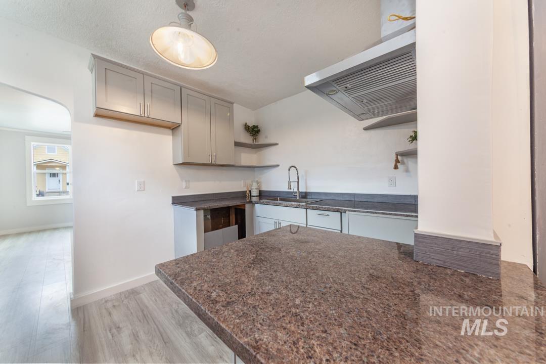 Kitchen featuring open shelves, light wood-style flooring, gray cabinetry, ventilation hood, and pendant lighting