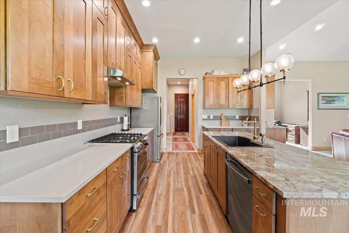 Kitchen featuring appliances with stainless steel finishes, under cabinet range hood, light wood-style floors, backsplash, and an island with sink