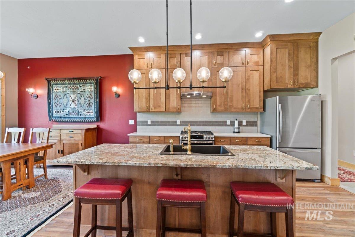Kitchen with appliances with stainless steel finishes, light wood-style floors, brown cabinets, backsplash, and recessed lighting