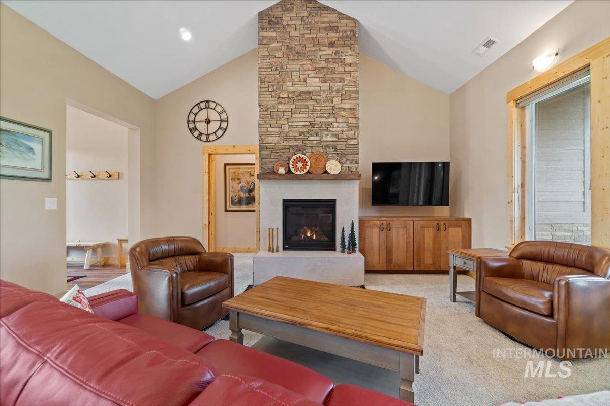 Living room with vaulted ceiling, a fireplace, and light carpet
