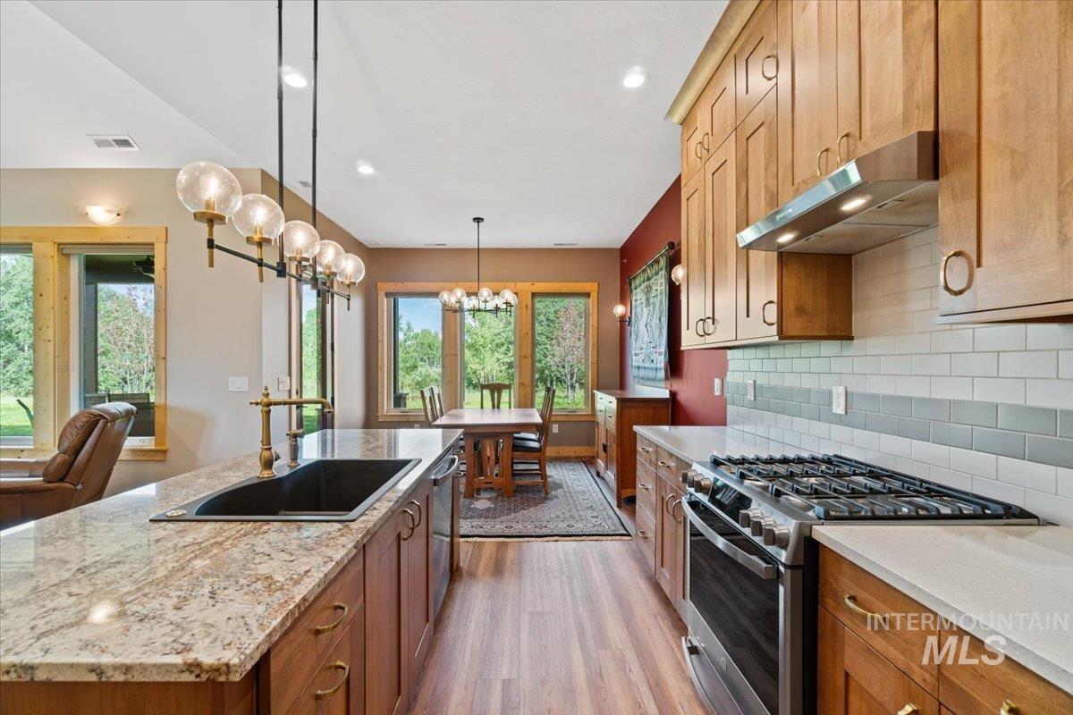 Kitchen with appliances with stainless steel finishes, under cabinet range hood, a chandelier, wood finished floors, and tasteful backsplash