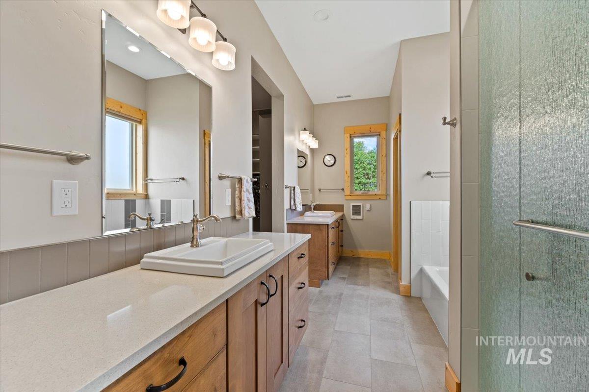 Full bath featuring an enclosed shower, plenty of natural light, two vanities, and a tub to relax in