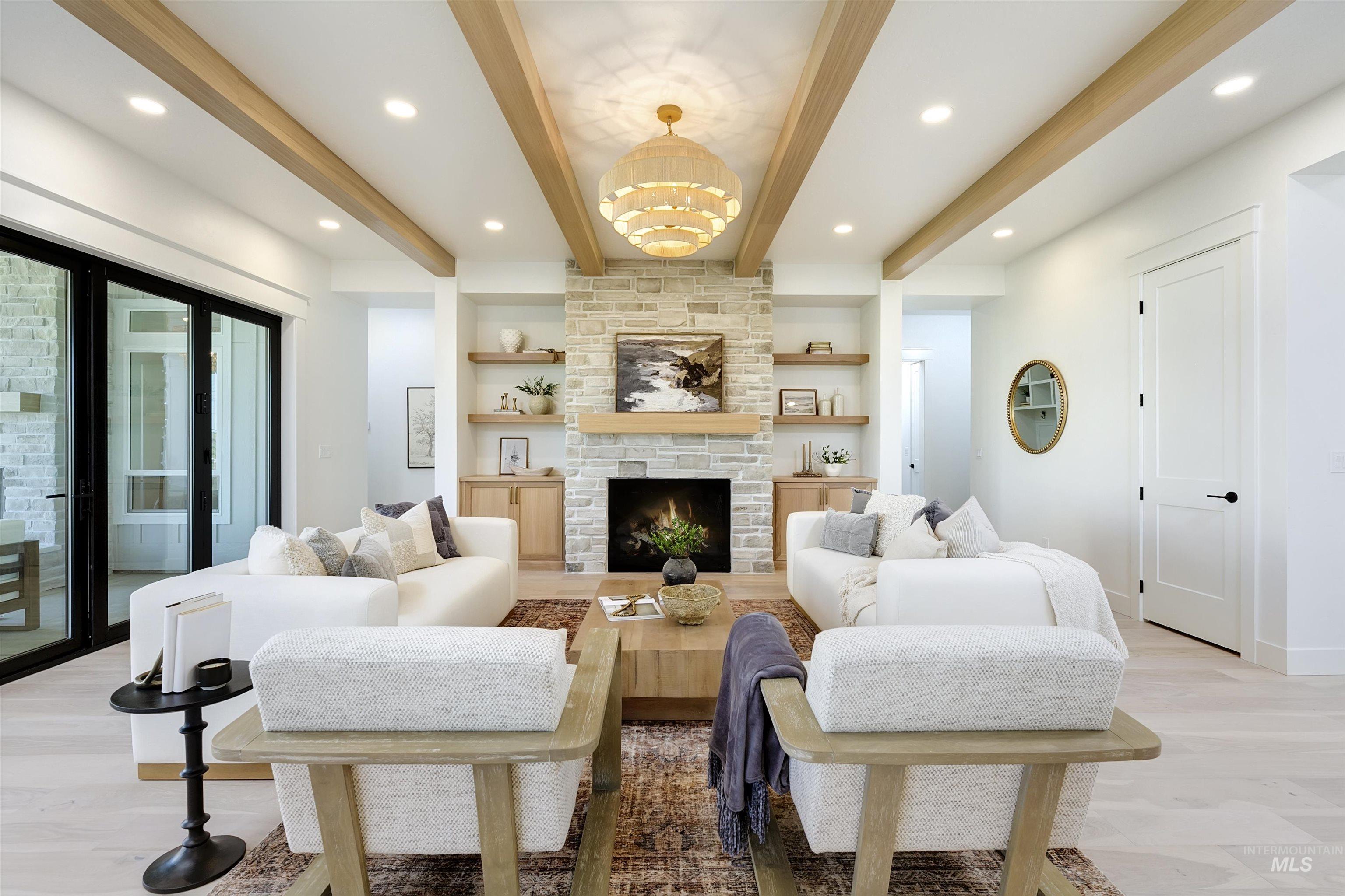 Living area featuring beam ceiling, a chandelier, a stone fireplace, built in shelves, and light wood-type flooring