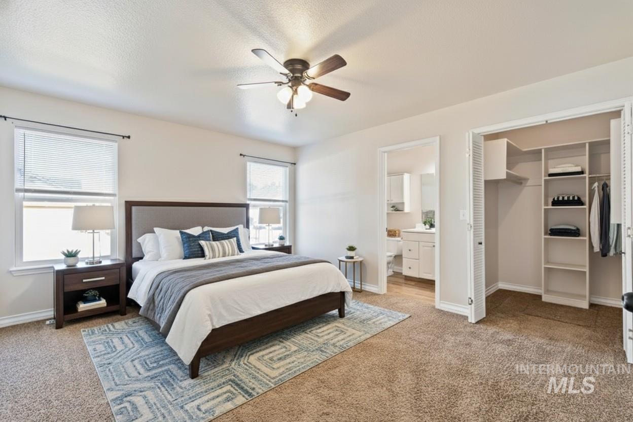 Bedroom with a walk in closet, light colored carpet, a ceiling fan, and ensuite bath