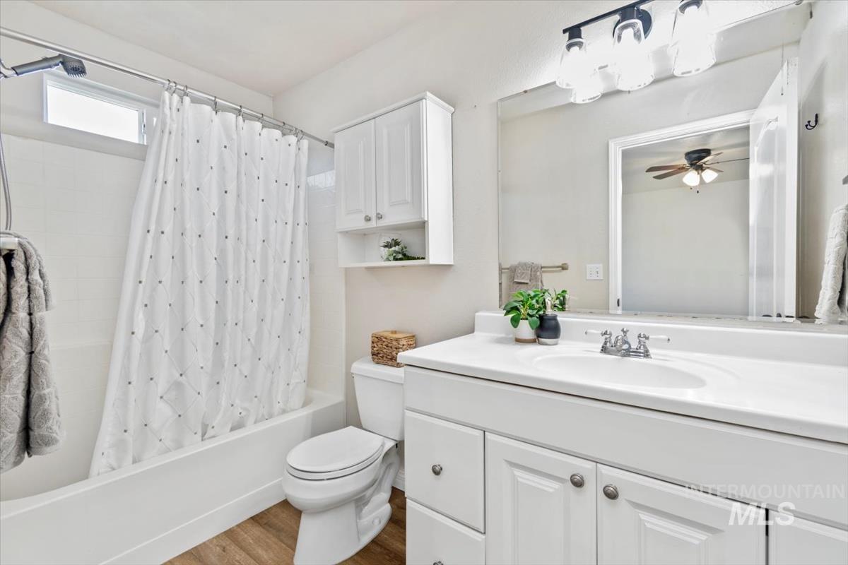 Bathroom with shower / tub combo, vanity, wood finished floors, and ceiling fan
