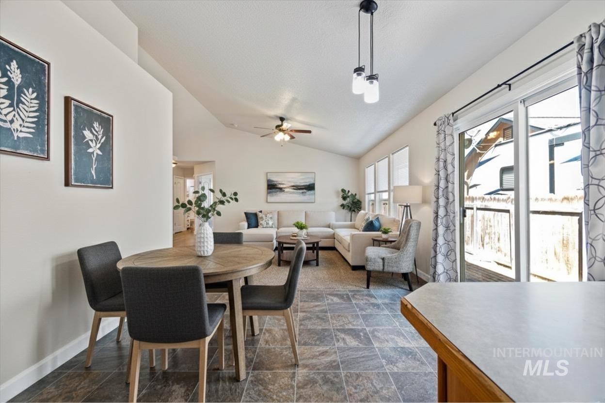 Dining area featuring vaulted ceiling, dark stone finish flooring, and ceiling fan