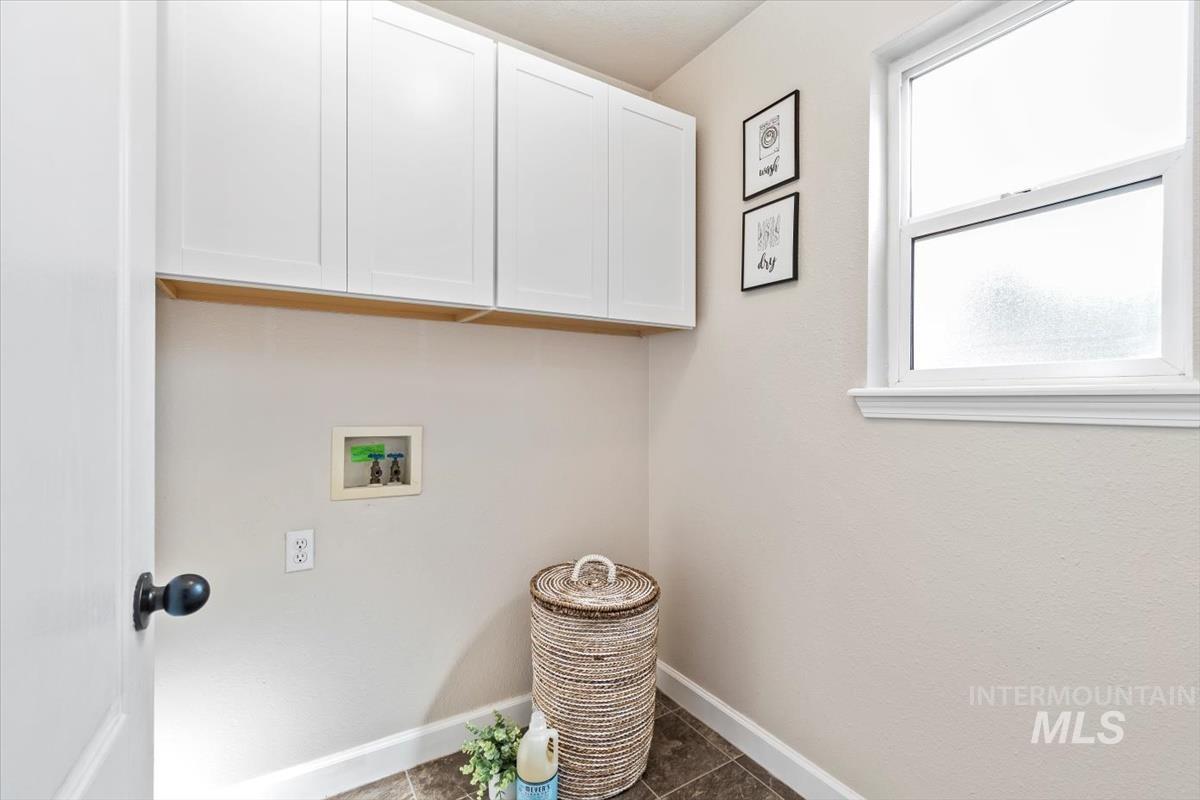 Laundry area featuring dark tile patterned flooring, cabinet space, and hookup for a washing machine