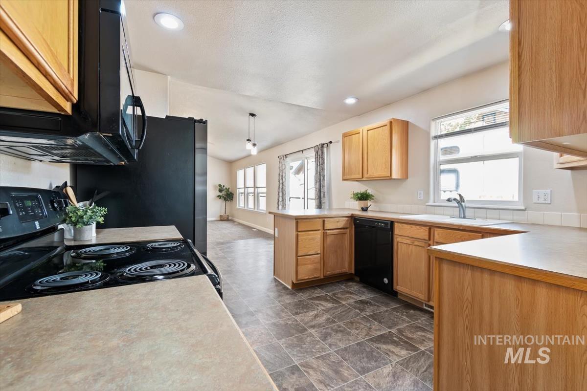 Kitchen featuring black appliances, light countertops, healthy amount of natural light, vaulted ceiling, and recessed lighting