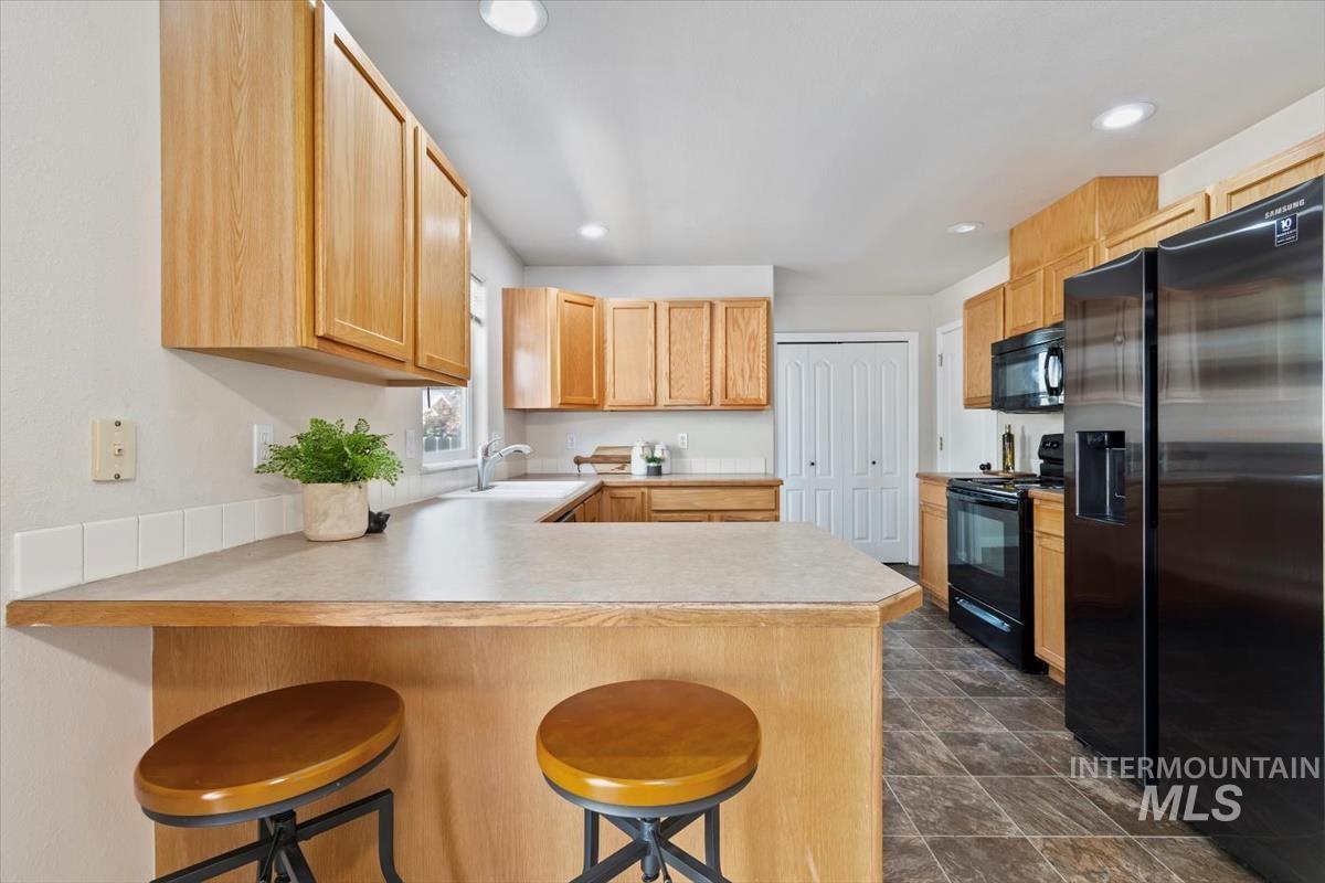 Kitchen featuring black appliances, a breakfast bar area, light countertops, a peninsula, and light brown cabinets