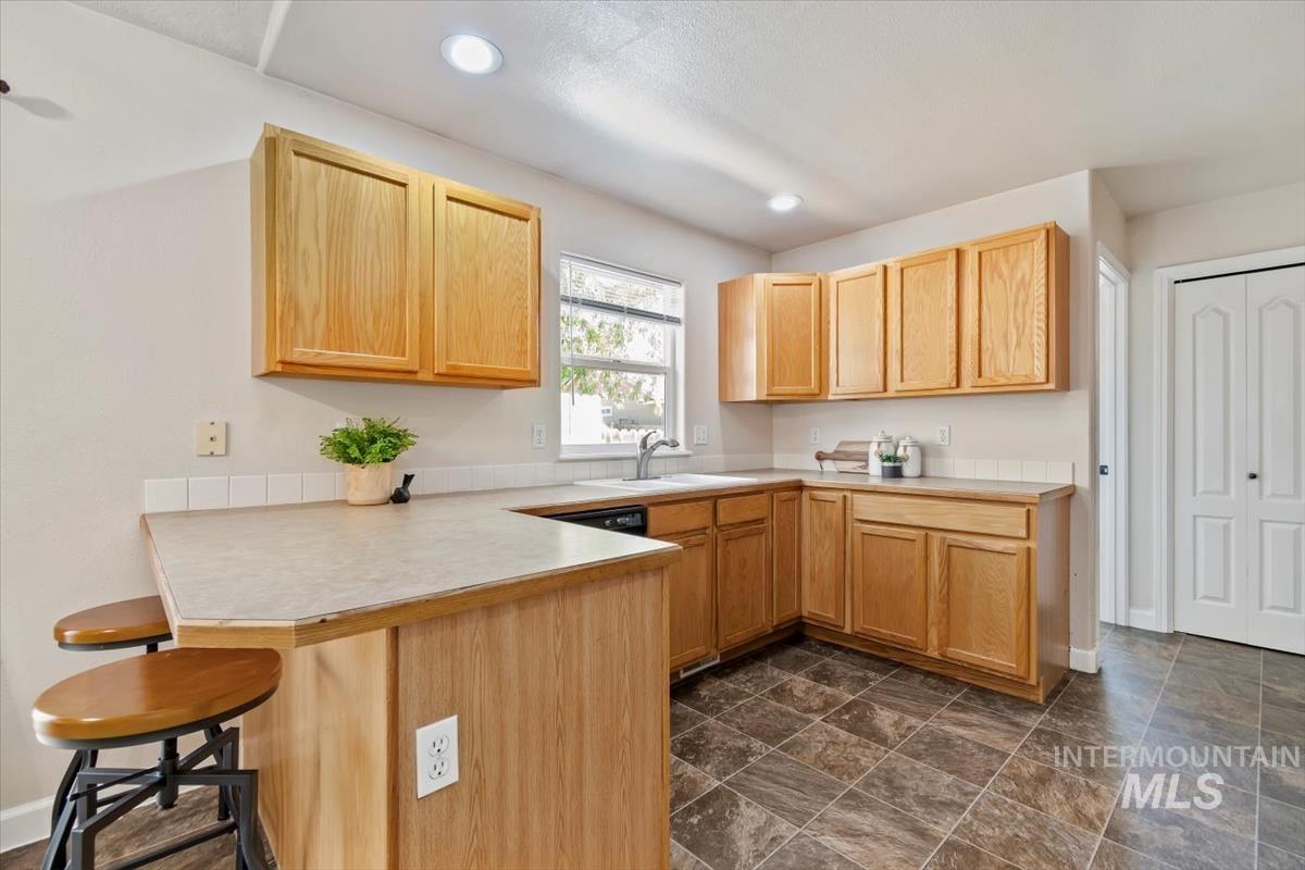 Kitchen featuring a breakfast bar area, a peninsula, light brown cabinets, light countertops, and recessed lighting