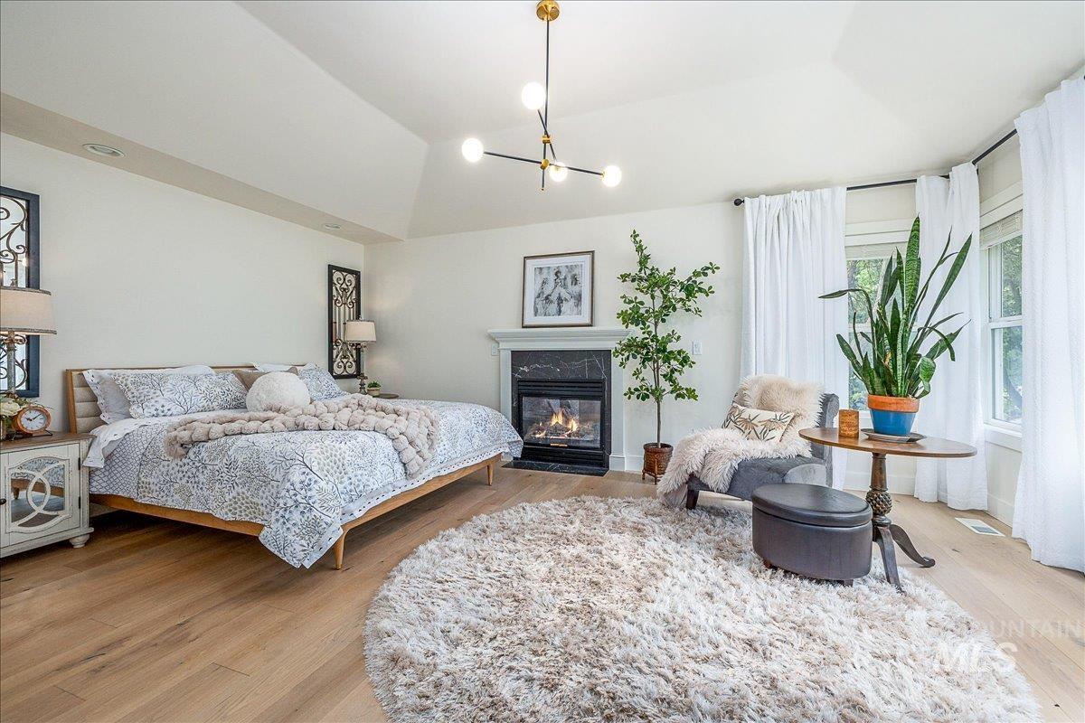 Bedroom with light wood-style floors, a premium fireplace, vaulted ceiling, and a chandelier