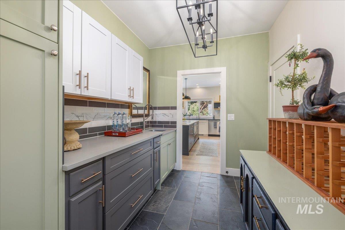 Kitchen featuring tasteful backsplash, stone tile floors, stainless steel dishwasher, white cabinets, and a chandelier