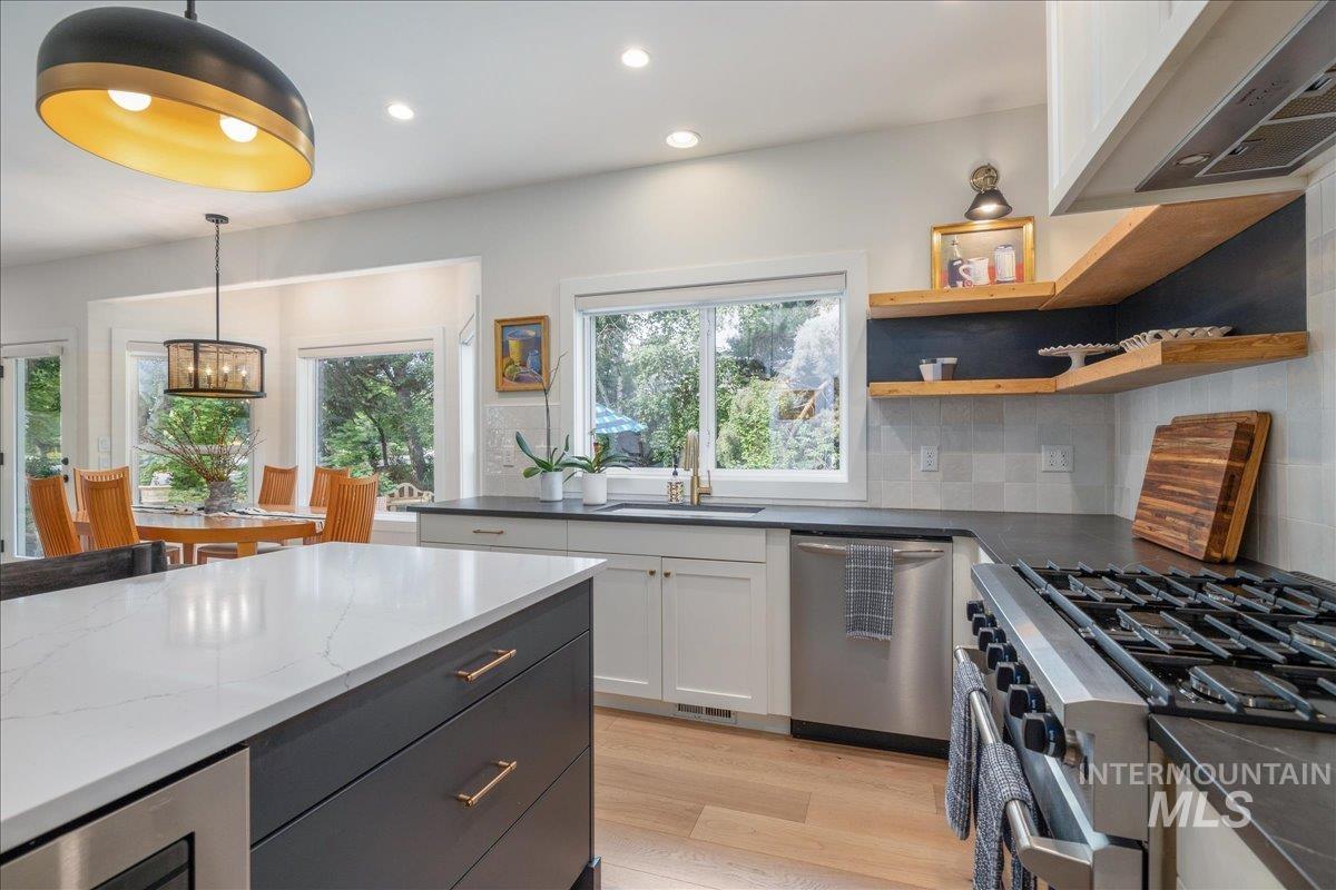 Kitchen featuring stainless steel appliances, dark cabinets, hanging light fixtures, recessed lighting, and light wood finished floors