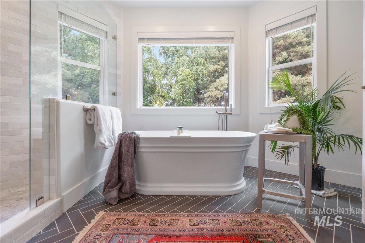 Full bathroom featuring a shower stall, a freestanding bath, and dark tile patterned flooring
