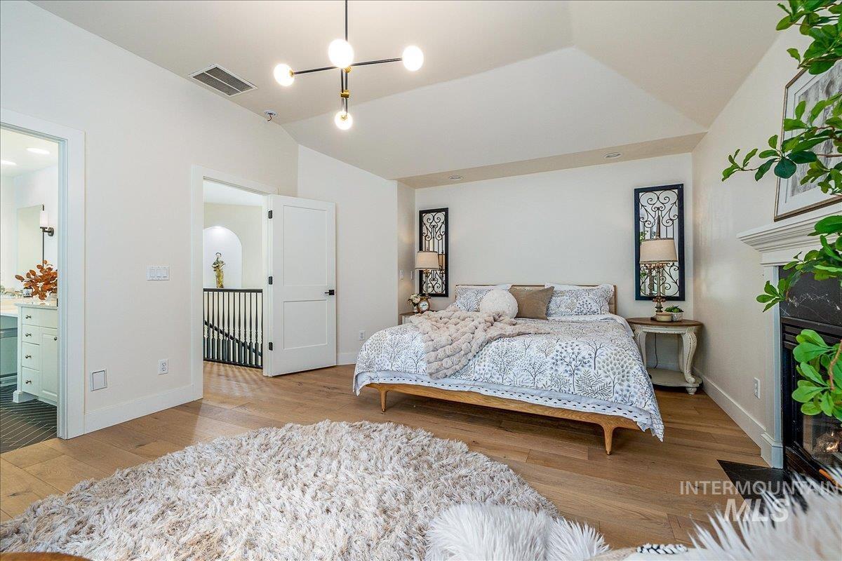Bedroom with light wood-style flooring, lofted ceiling, and ensuite bath