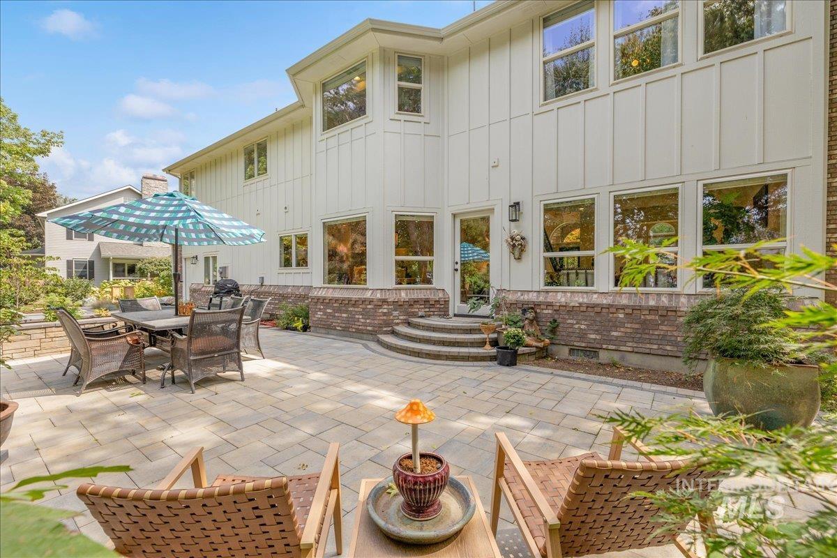 Back of property with board and batten siding, a patio area, brick siding, entry steps, and outdoor dining space