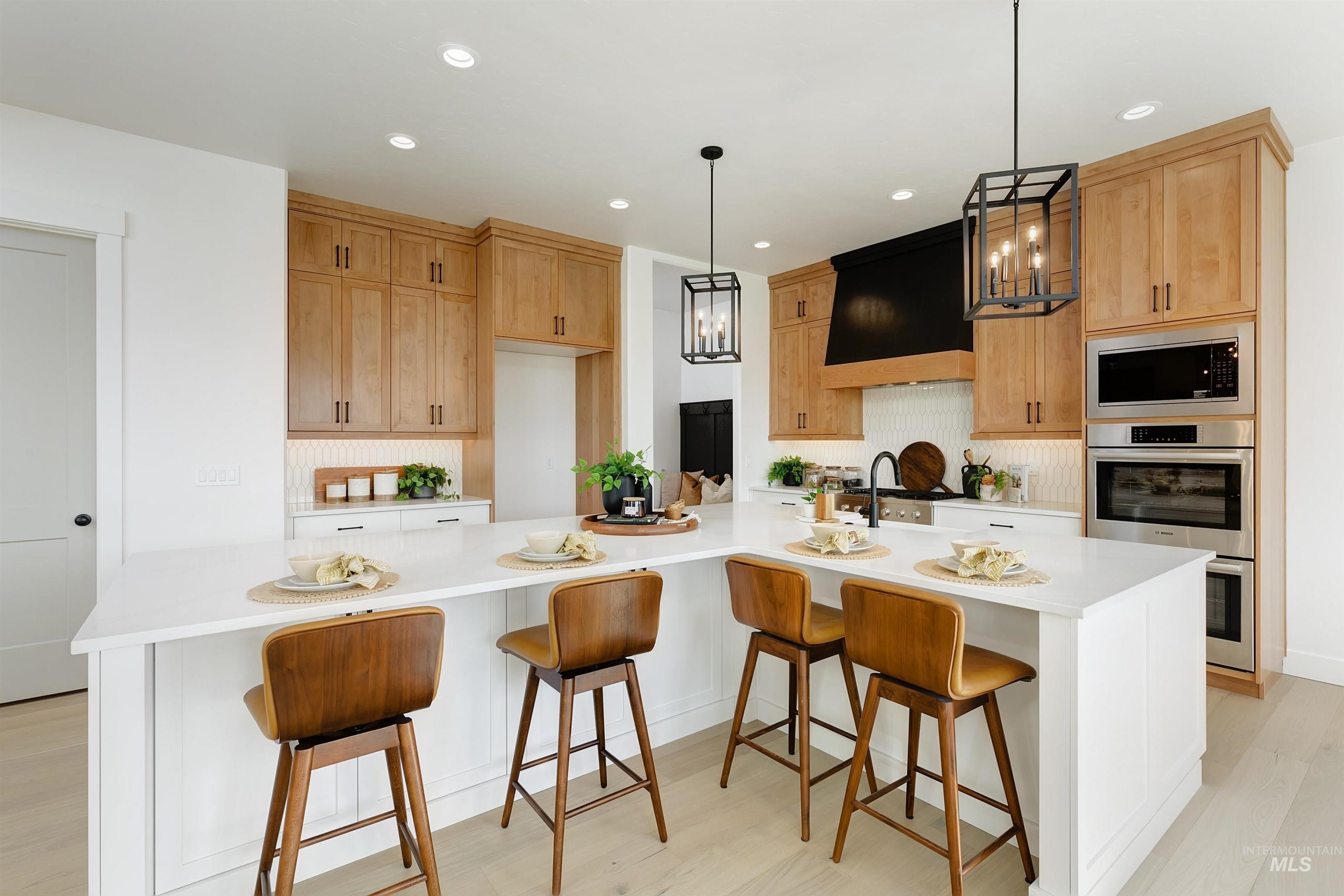 Kitchen with a breakfast bar area, pendant lighting, recessed lighting, custom range hood, and appliances with stainless steel finishes