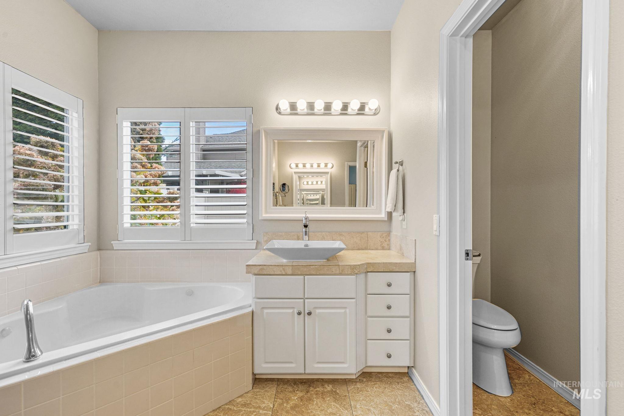 Full bath with vanity, a bath, and light tile patterned flooring