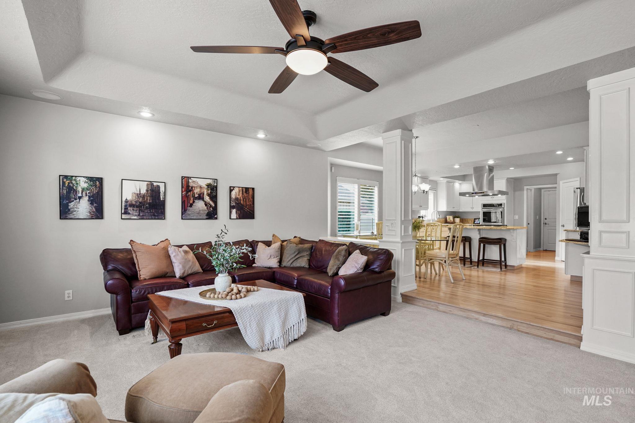 Living area featuring decorative columns, a tray ceiling, recessed lighting, light colored carpet, and ceiling fan
