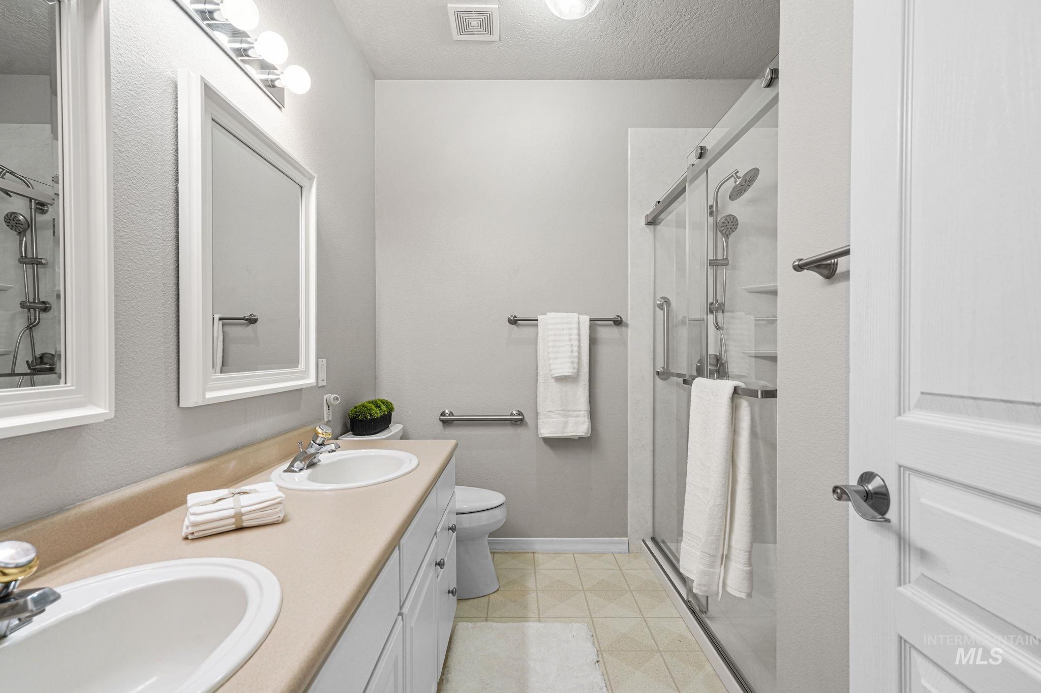 Full bathroom featuring a textured ceiling, a shower stall, and double vanity
