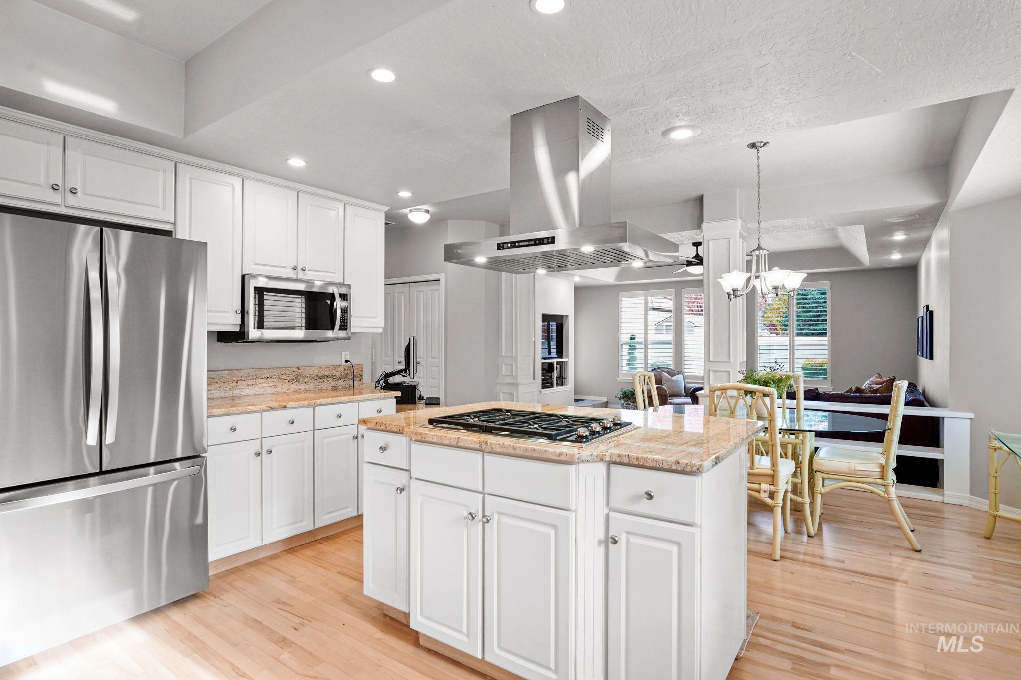 Kitchen with stainless steel appliances, recessed lighting, white cabinets, light wood-type flooring, and light stone counters
