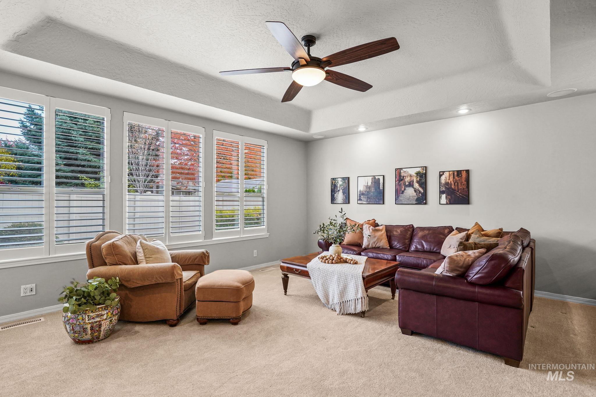 Carpeted living area featuring a raised ceiling, a textured ceiling, and a ceiling fan
