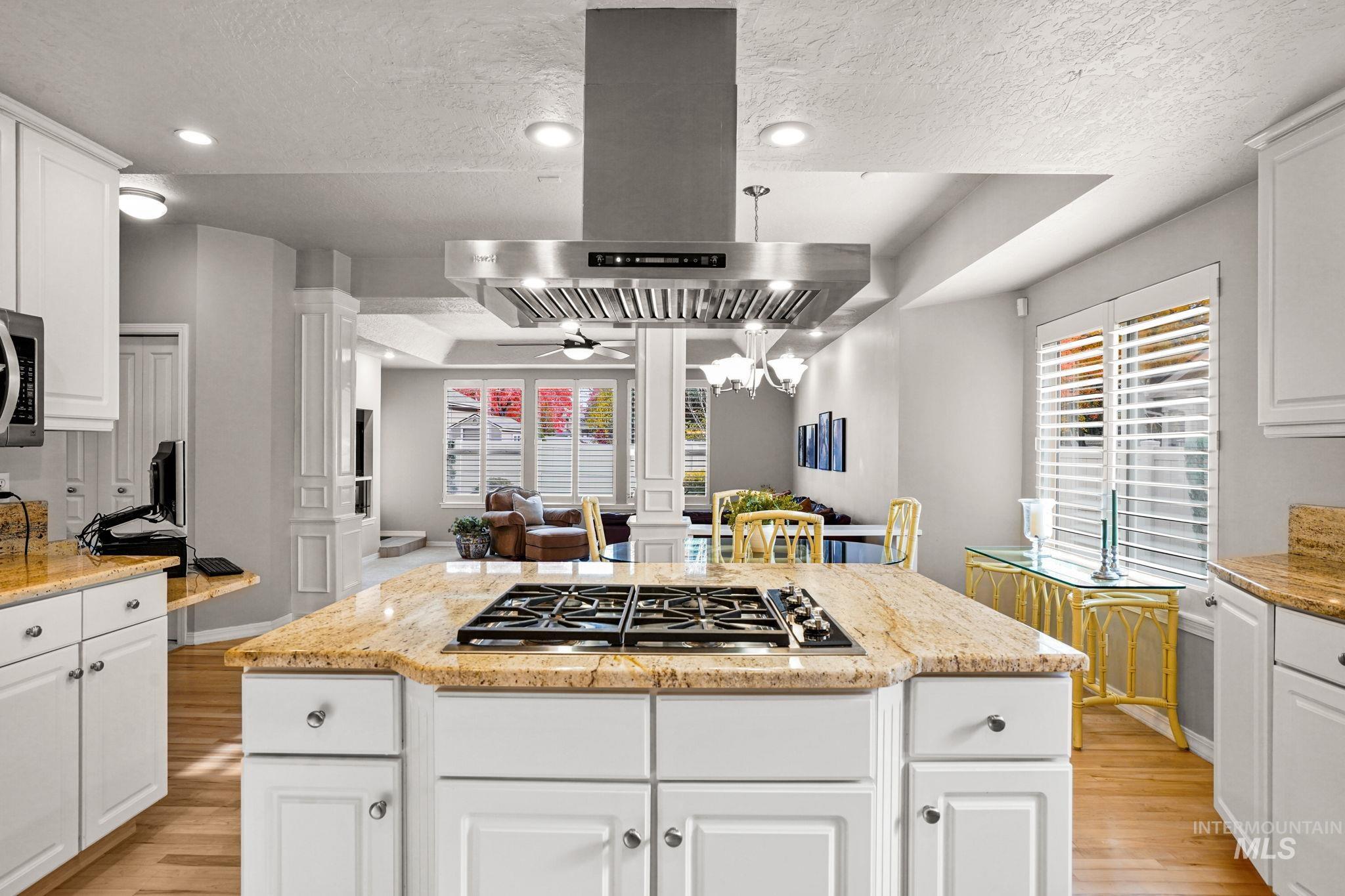 Kitchen featuring white cabinetry, ornate columns, island range hood, light stone countertops, and a textured ceiling