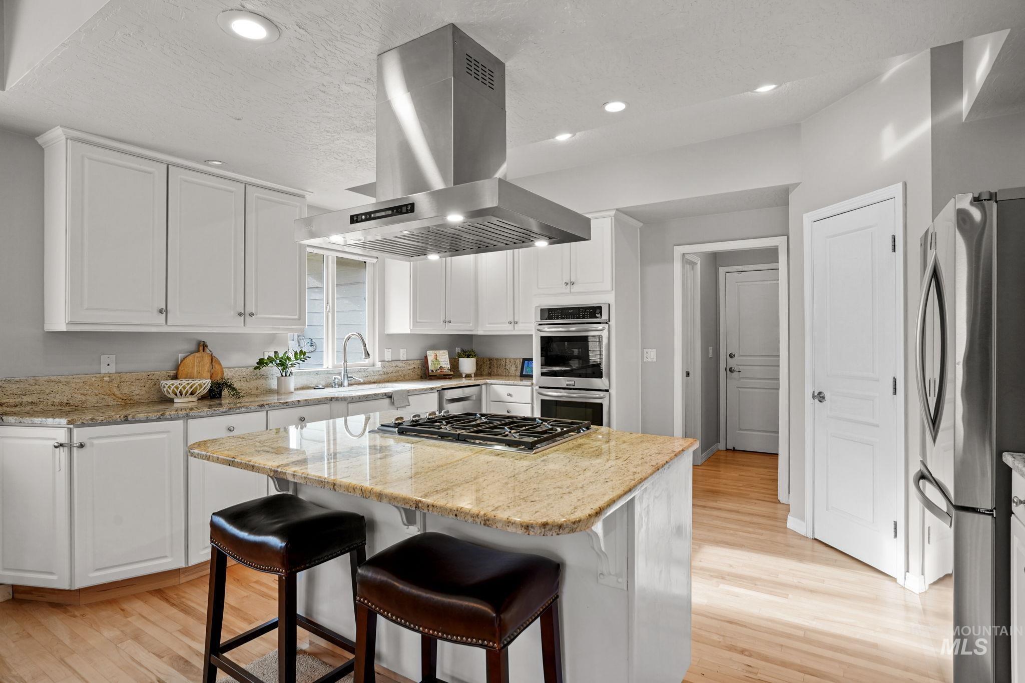 Kitchen with light wood-style flooring, white cabinets, light stone counters, a kitchen breakfast bar, and island exhaust hood