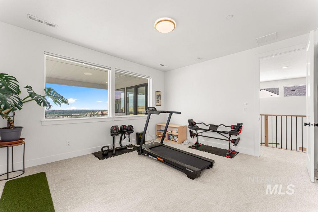 Bright room with large windows, carpet flooring, a ceiling-mounted light fixture, and an open doorway leading to a hallway with a metal railing