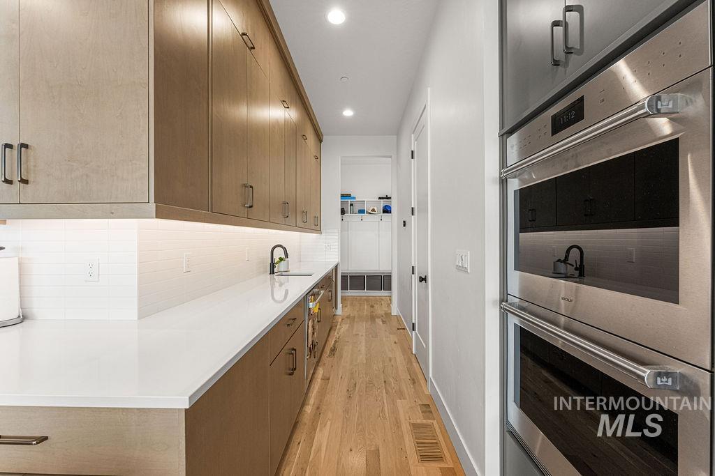 Modern kitchen with light wood-finish cabinetry, integrated stainless steel double ovens, and wood-finish flooring