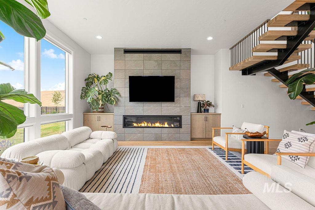 Living area featuring a floor-to-ceiling tiled fireplace with an integrated linear firebox, light wood-finish flooring, and a contemporary open staircase with metal railings