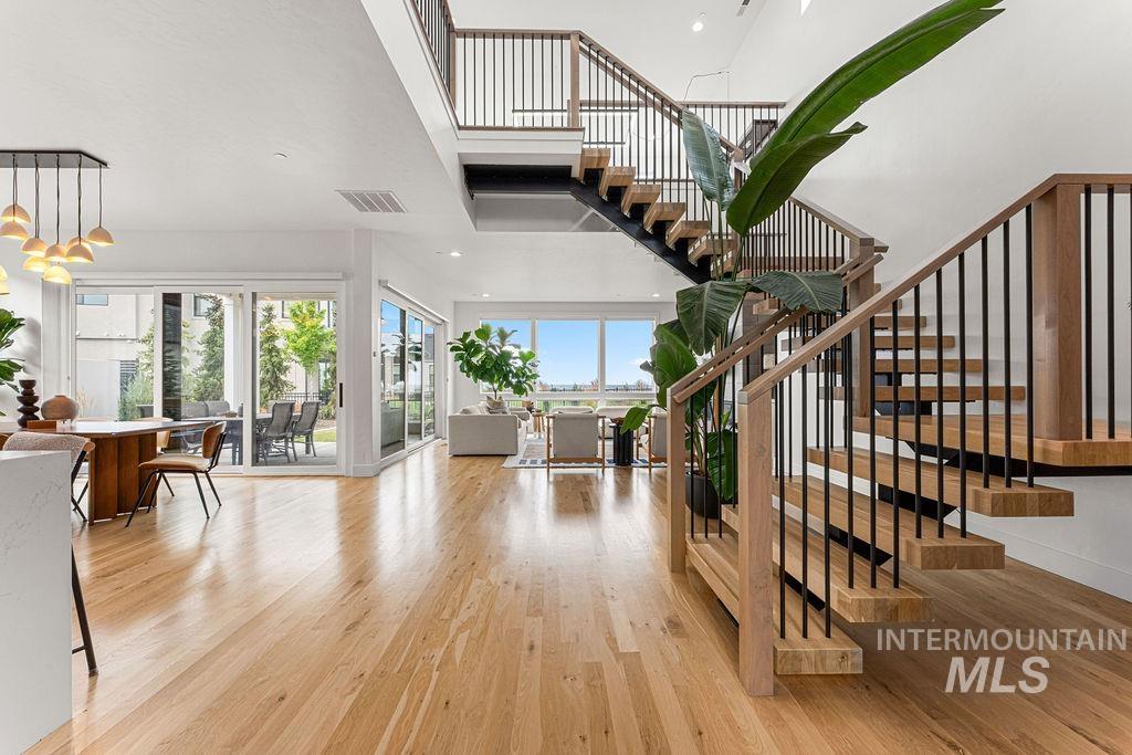 Open-concept living area featuring light wood-finish flooring, a two-story exposed staircase with black metal balusters, and multiple large sliding glass doors
