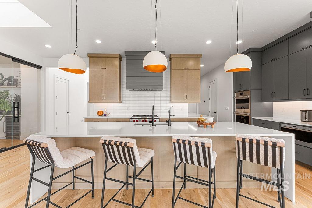 Spacious kitchen featuring a large central island with seating, a skylight, wood-finish flooring, and a mix of light wood and dark gray cabinetry