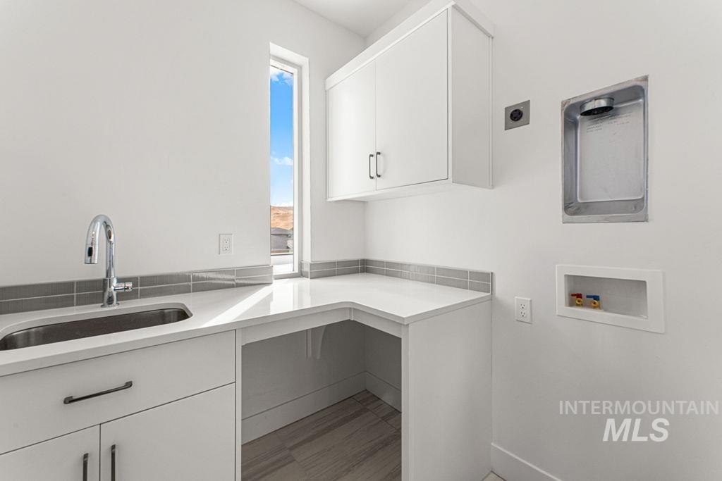 Laundry room featuring a utility sink with a chrome faucet, white cabinetry, and a light-colored countertop