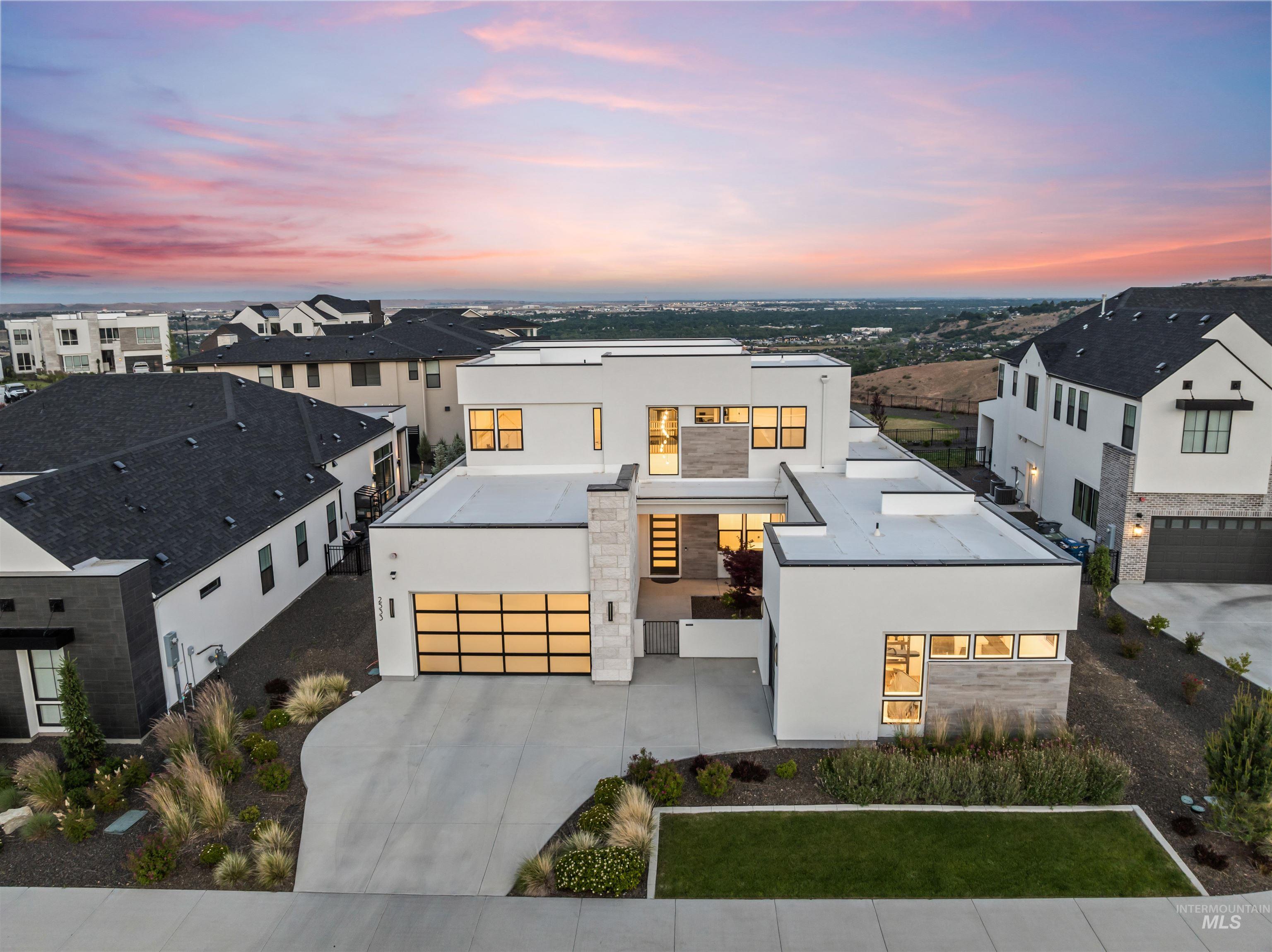 Contemporary residence featuring a clean white exterior, stone accents, multiple large windows, a glass-paneled garage door, and a concrete driveway