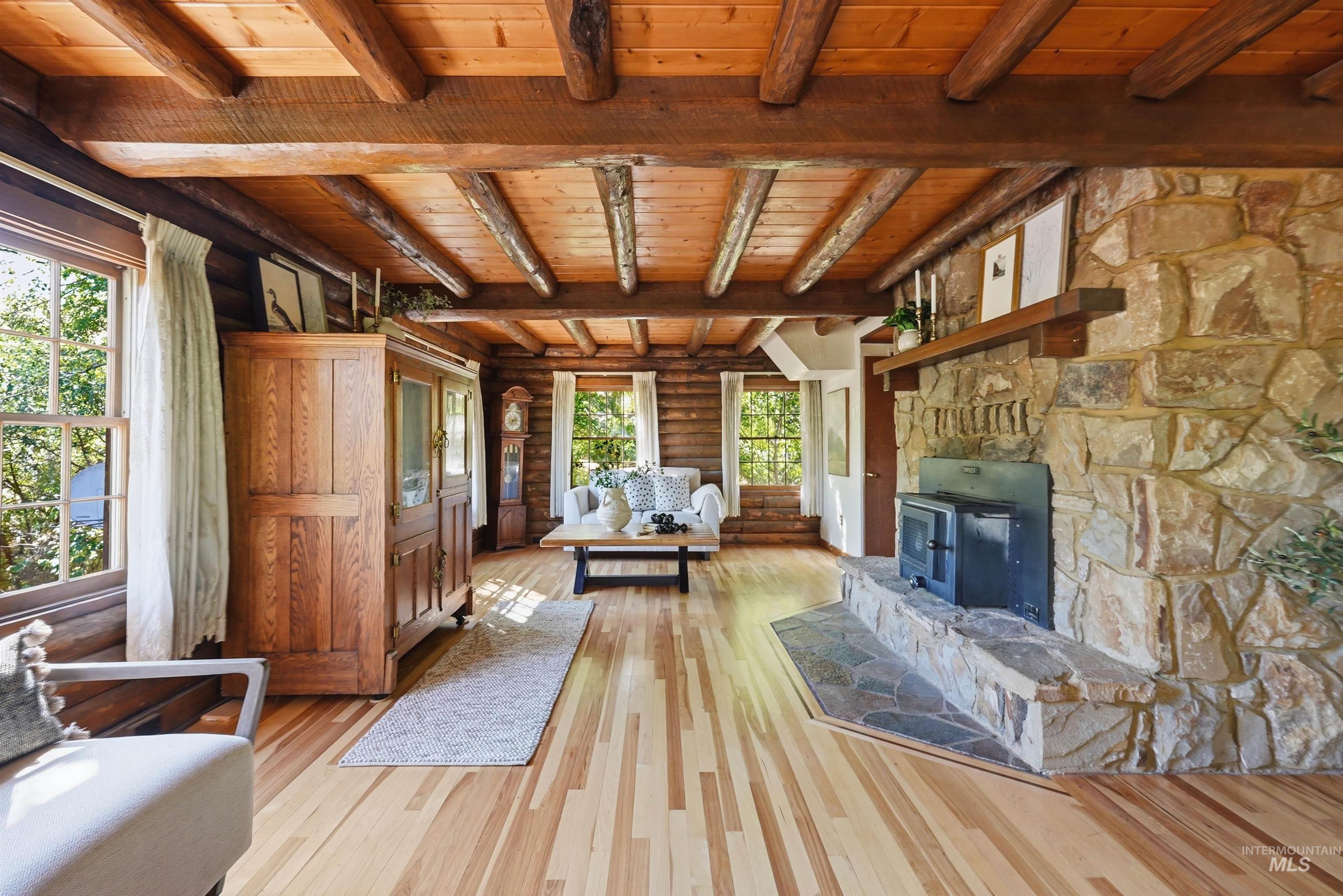 Living area featuring a stone fireplace with a wood-burning stove insert, exposed wood beam ceiling, and light wood-finish flooring