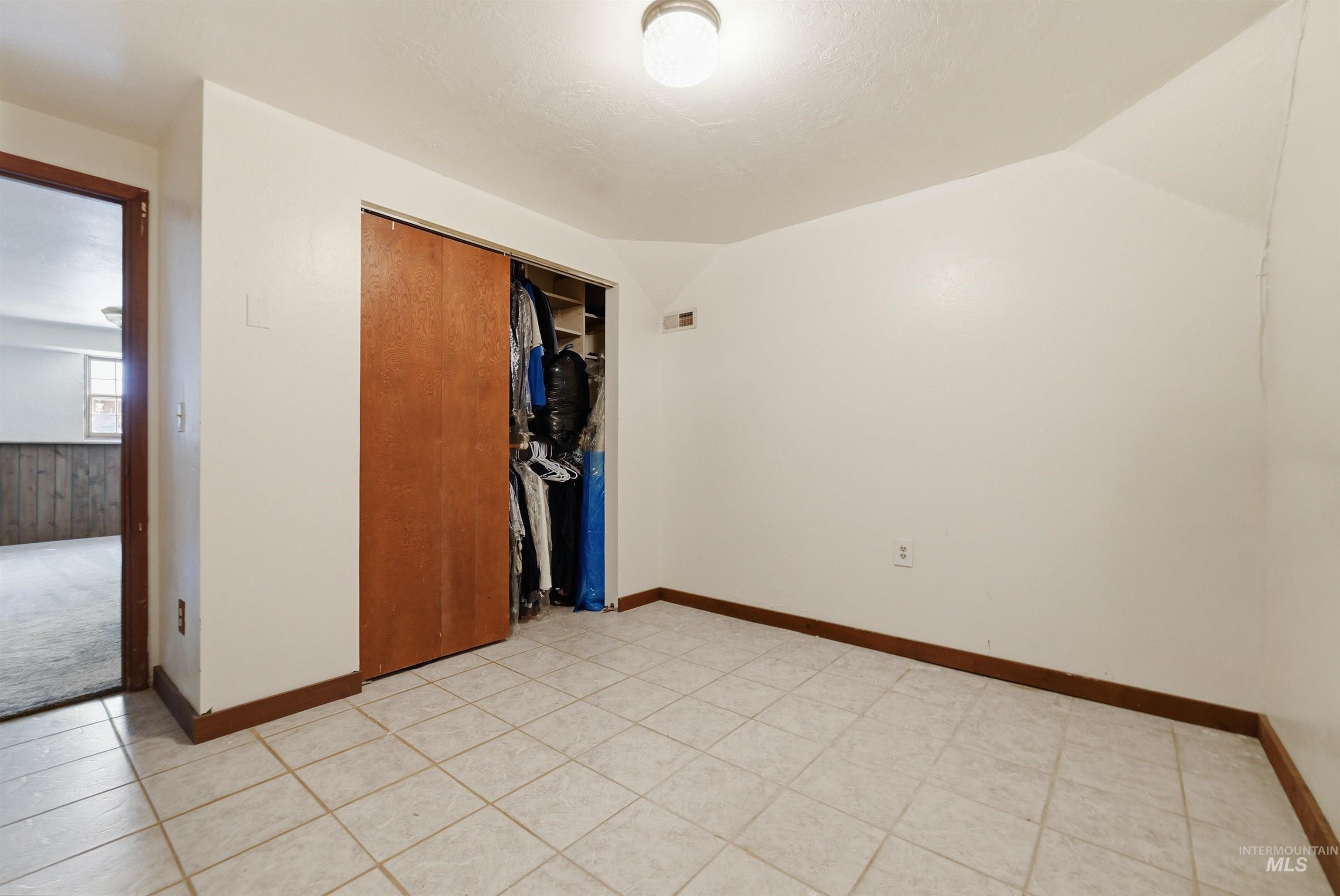Room featuring neutral-toned square tile flooring, a built-in closet with wood-finish sliding doors, and white painted walls