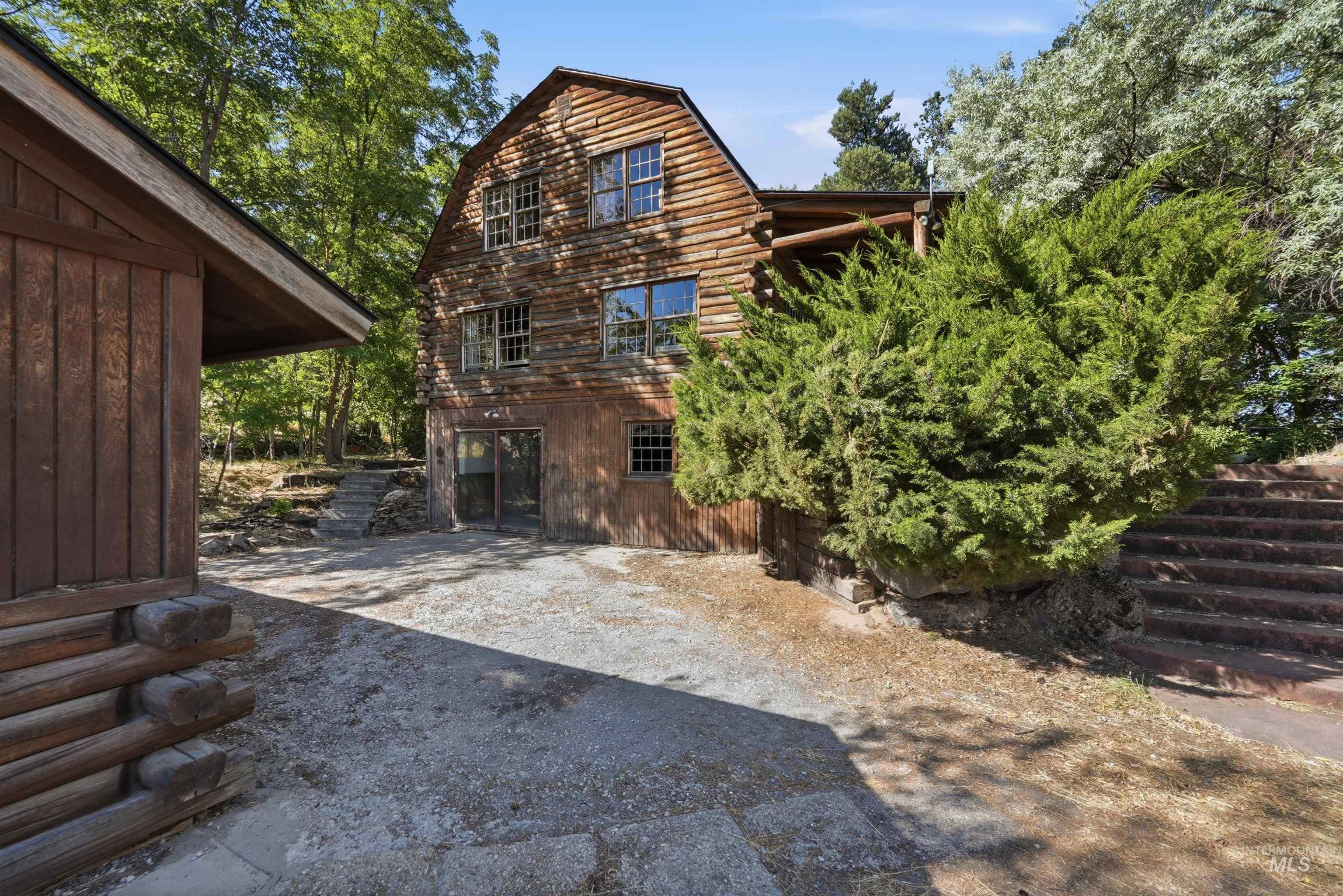 Multi-story structure featuring natural wood siding and multiple windows, complemented by a detached log cabin-style outbuilding