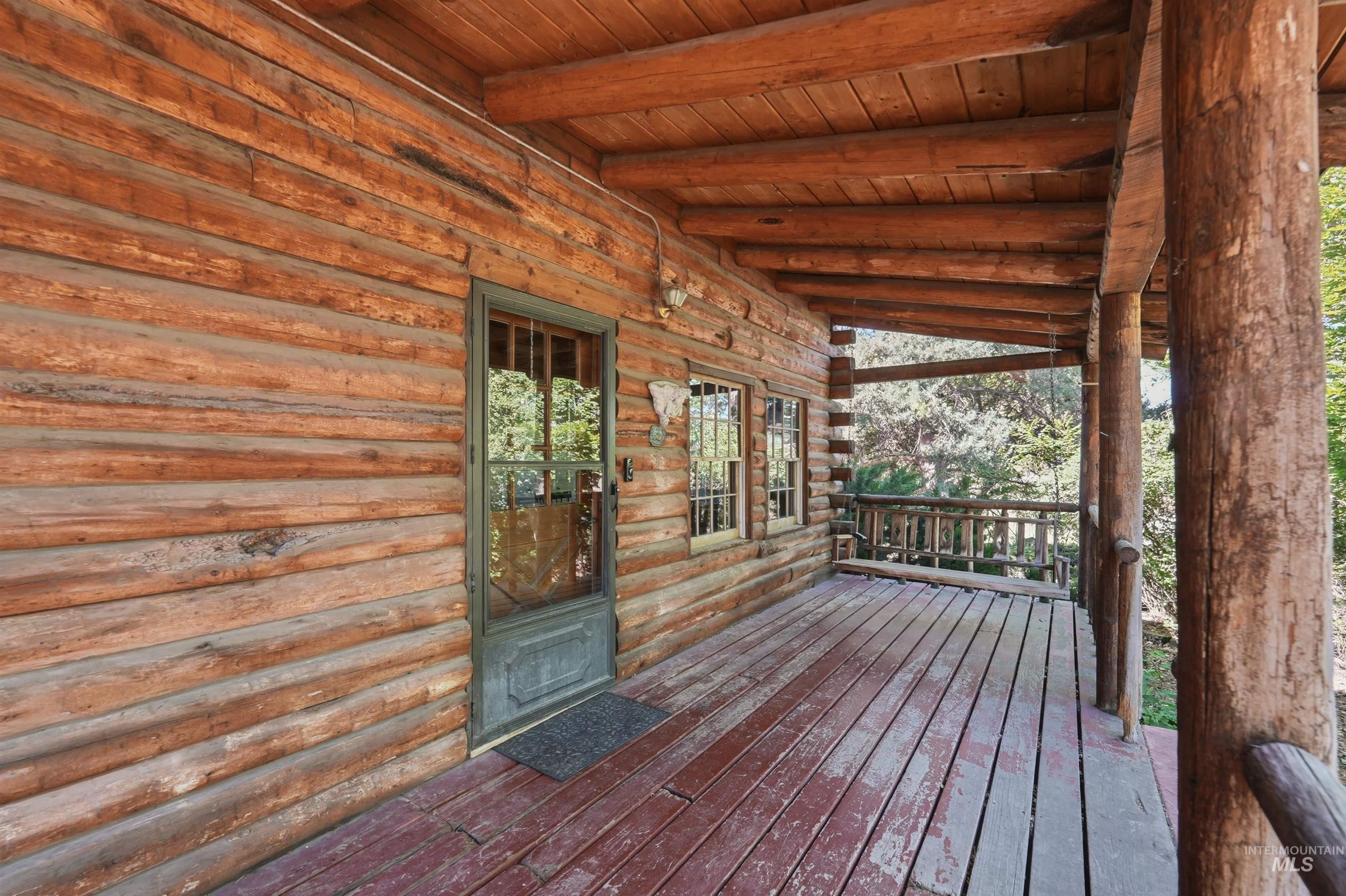 Expansive covered porch featuring natural log construction, exposed beam ceiling, wood-plank flooring, and a screened door