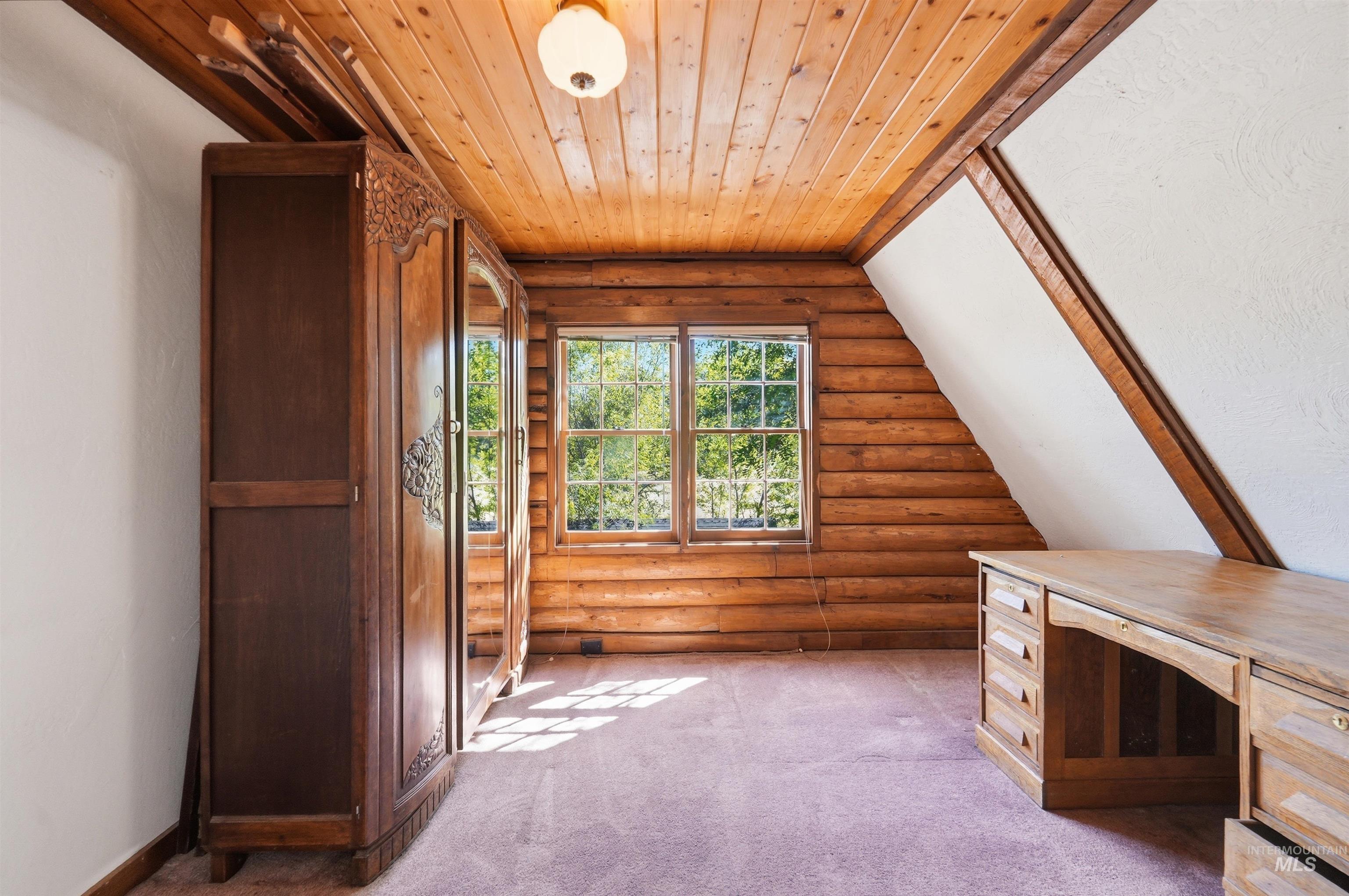 Attic space featuring wood-paneled walls and ceiling, twin-pane windows, and sloped white walls