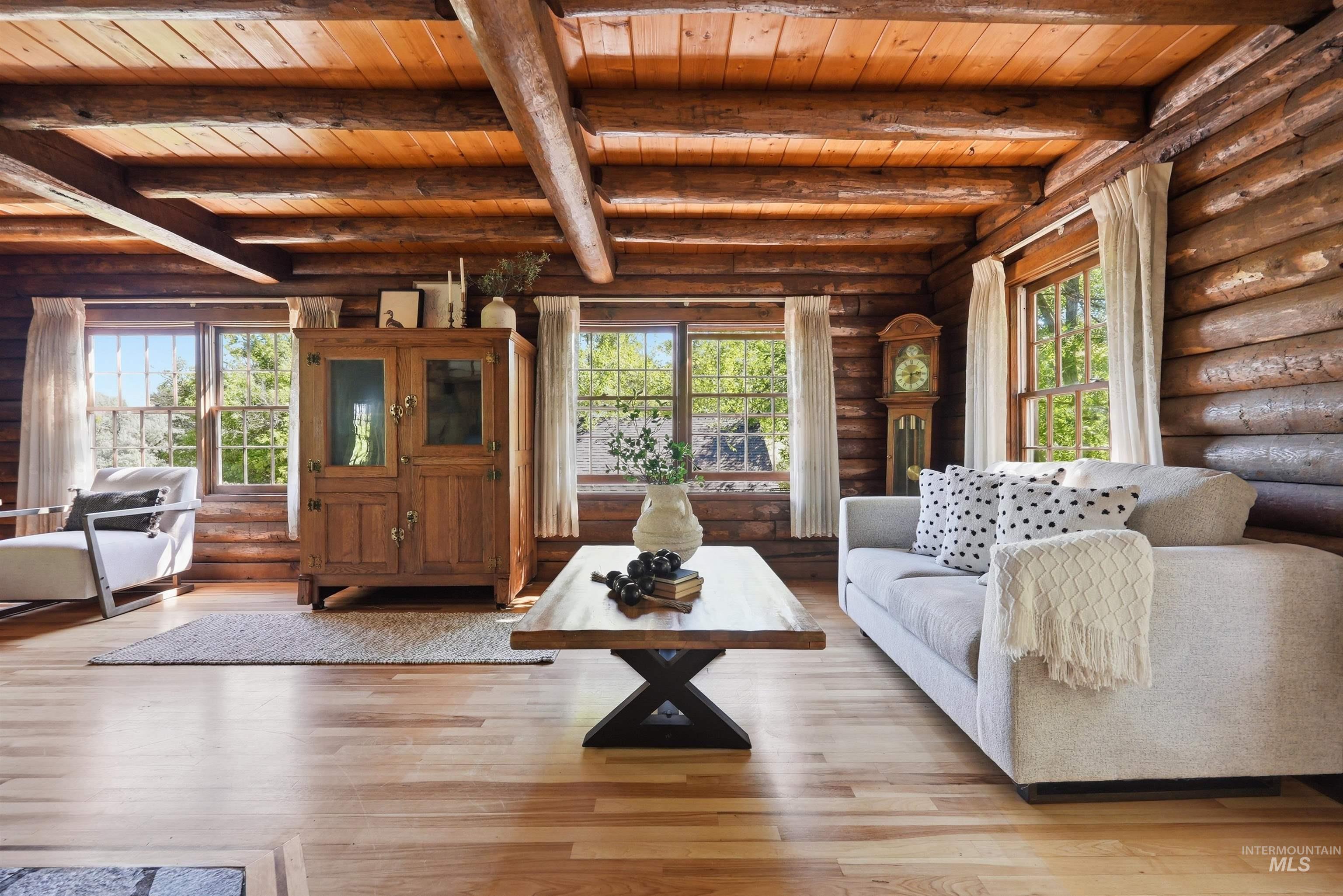 Living area featuring natural log walls, exposed wood-beam ceilings, natural wood-finish flooring, and multiple window openings
