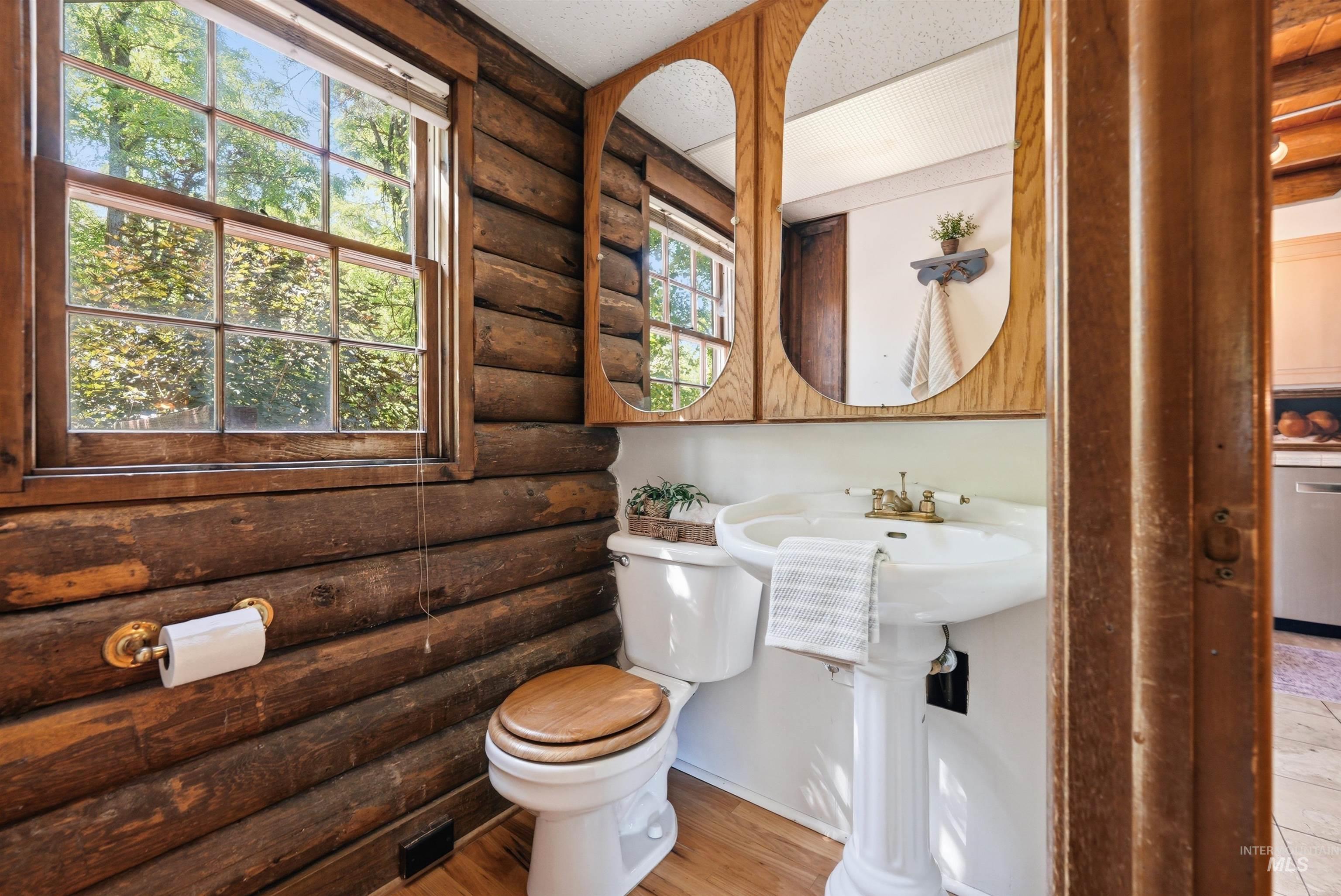 main level 1/2  bathroom with a multi-pane window, pedestal sink, and wood-finish flooring