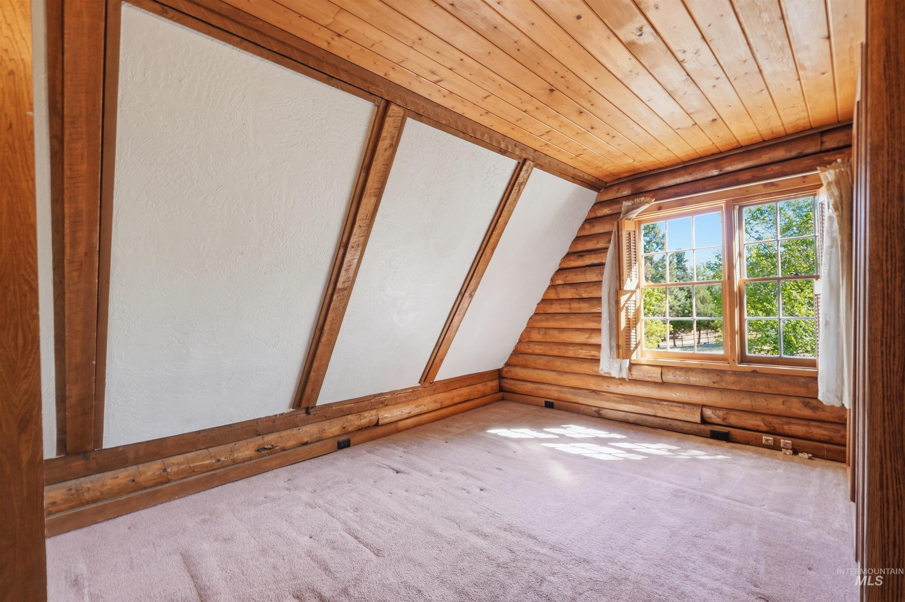 Room featuring wood-planked walls and ceiling, a window with exterior views, and sloped freshly painted walls with wood framing