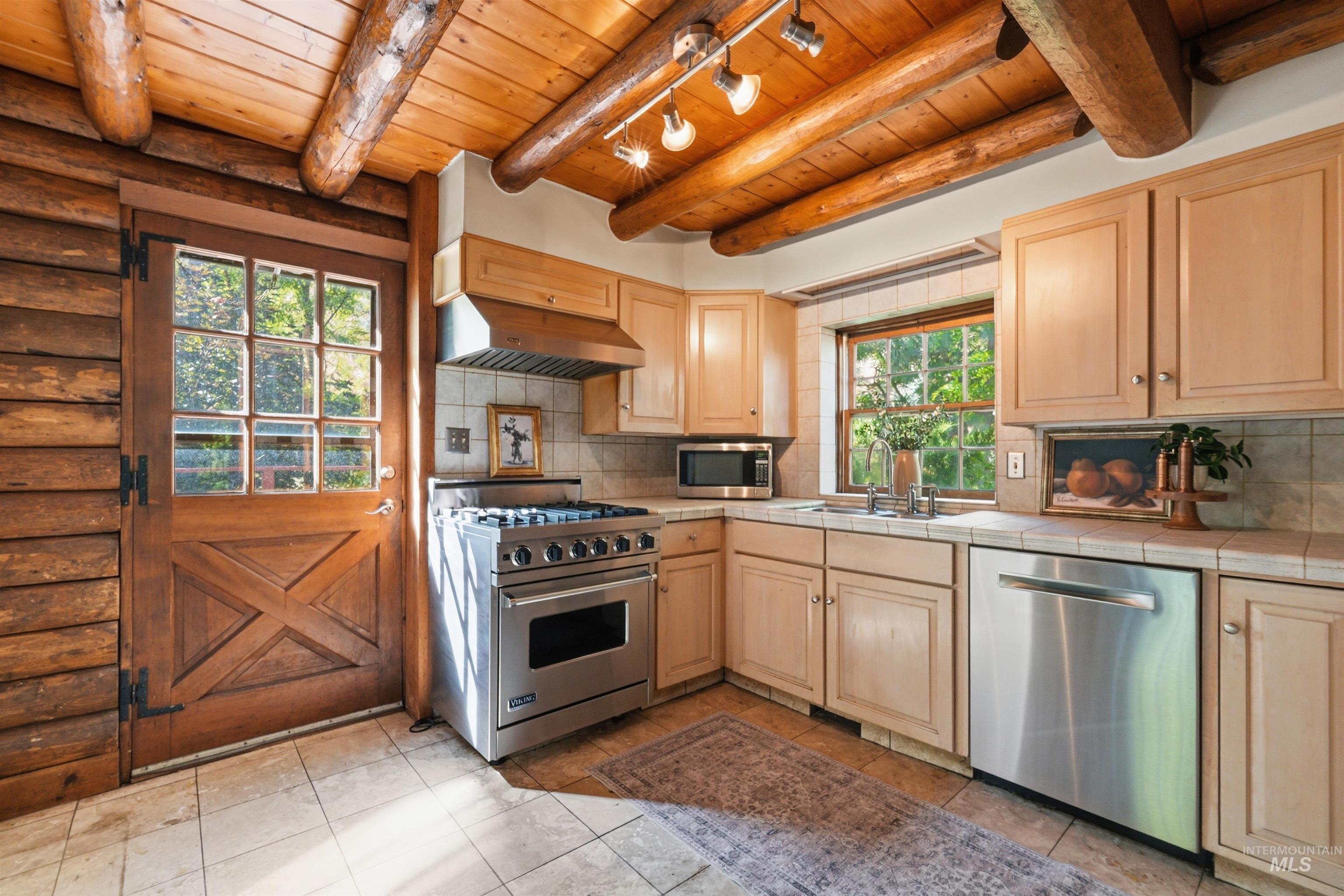 Kitchen featuring wood-paneled walls, exposed wood beams, light wood cabinetry, a stainless steel range, and tile flooring