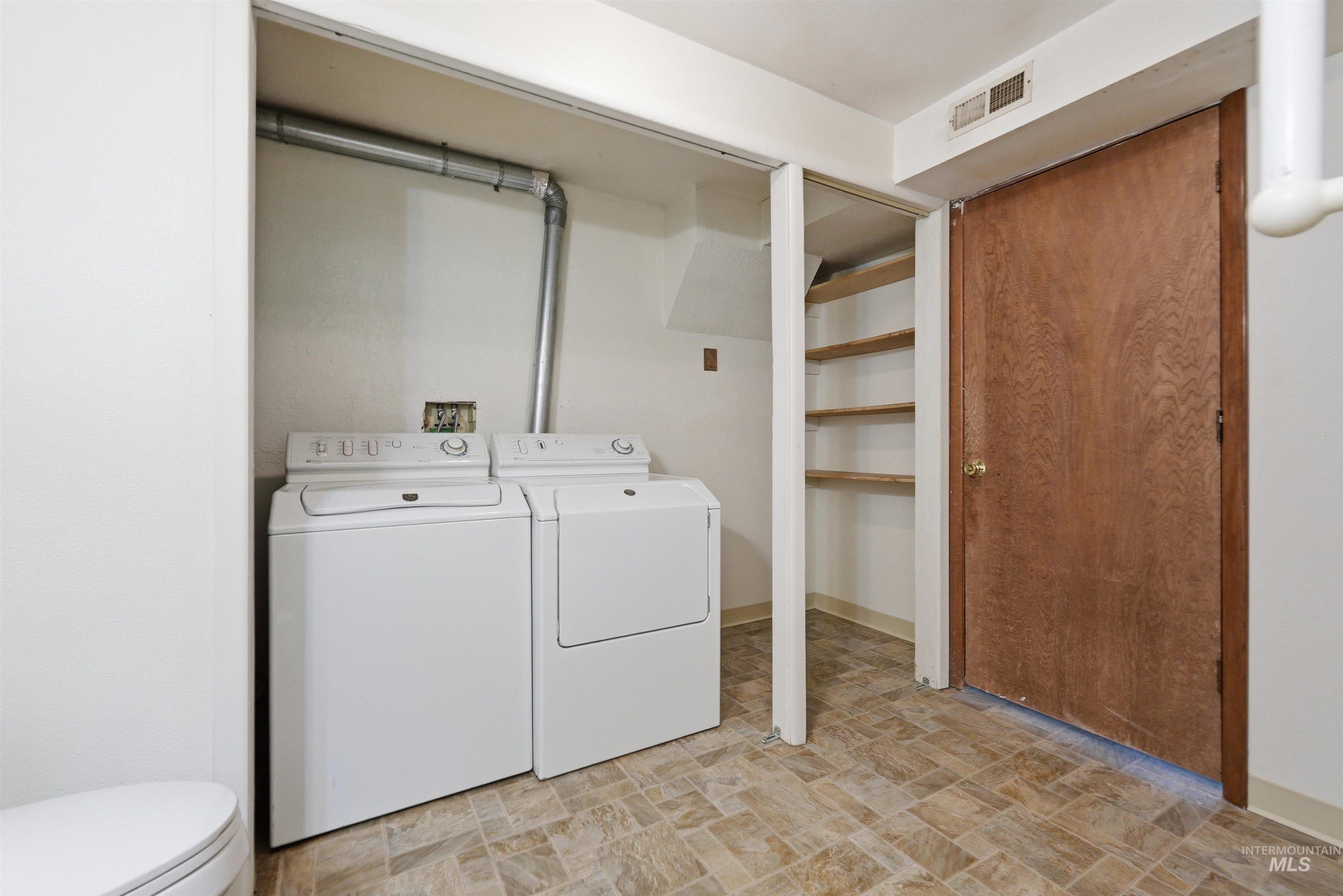 Laundry area featuring a side-by-side washer and dryer, built-in wooden shelving, brown wood-finish door, and patterned floor tile