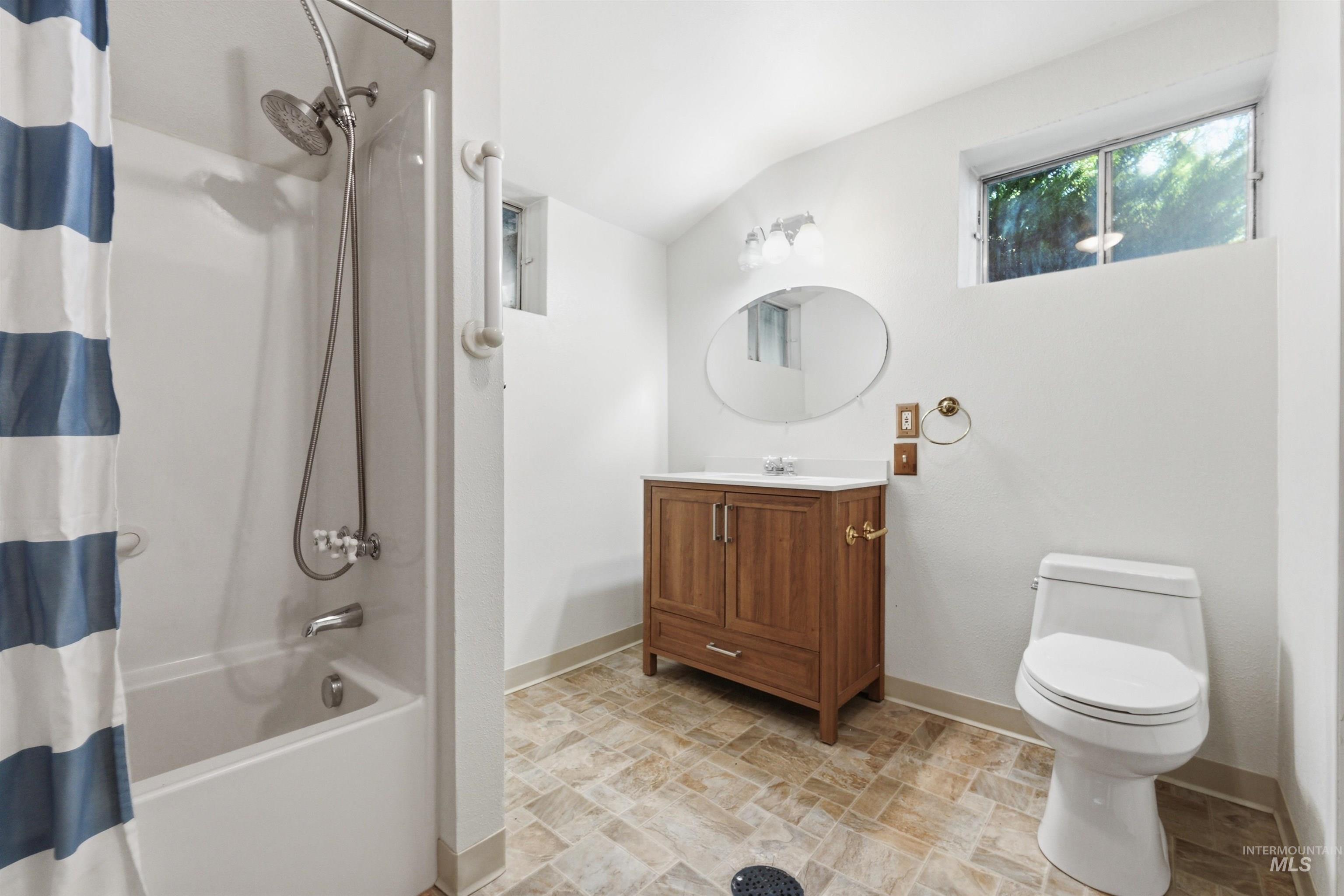 Bathroom featuring a white bathtub with a shower system, a wood-finish vanity with a white countertop and basin, an oval mirror, and a toilet